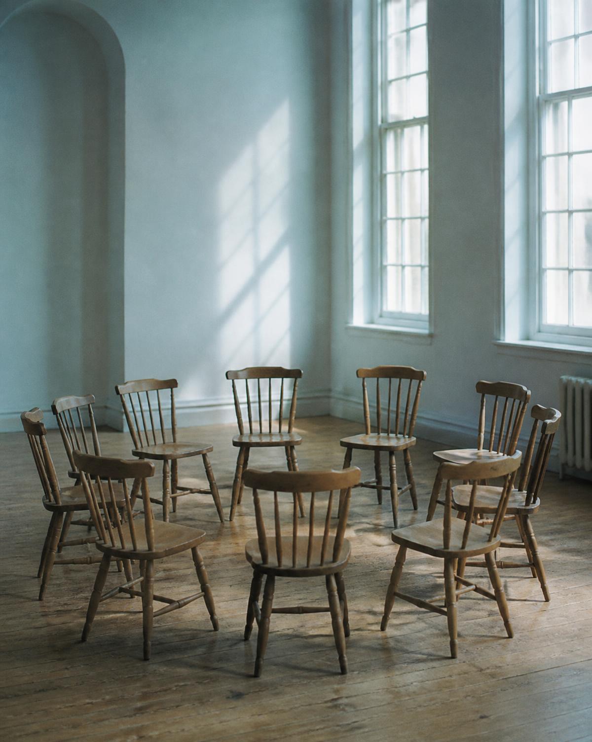A circle of simple wooden chairs in a bright, airy room
